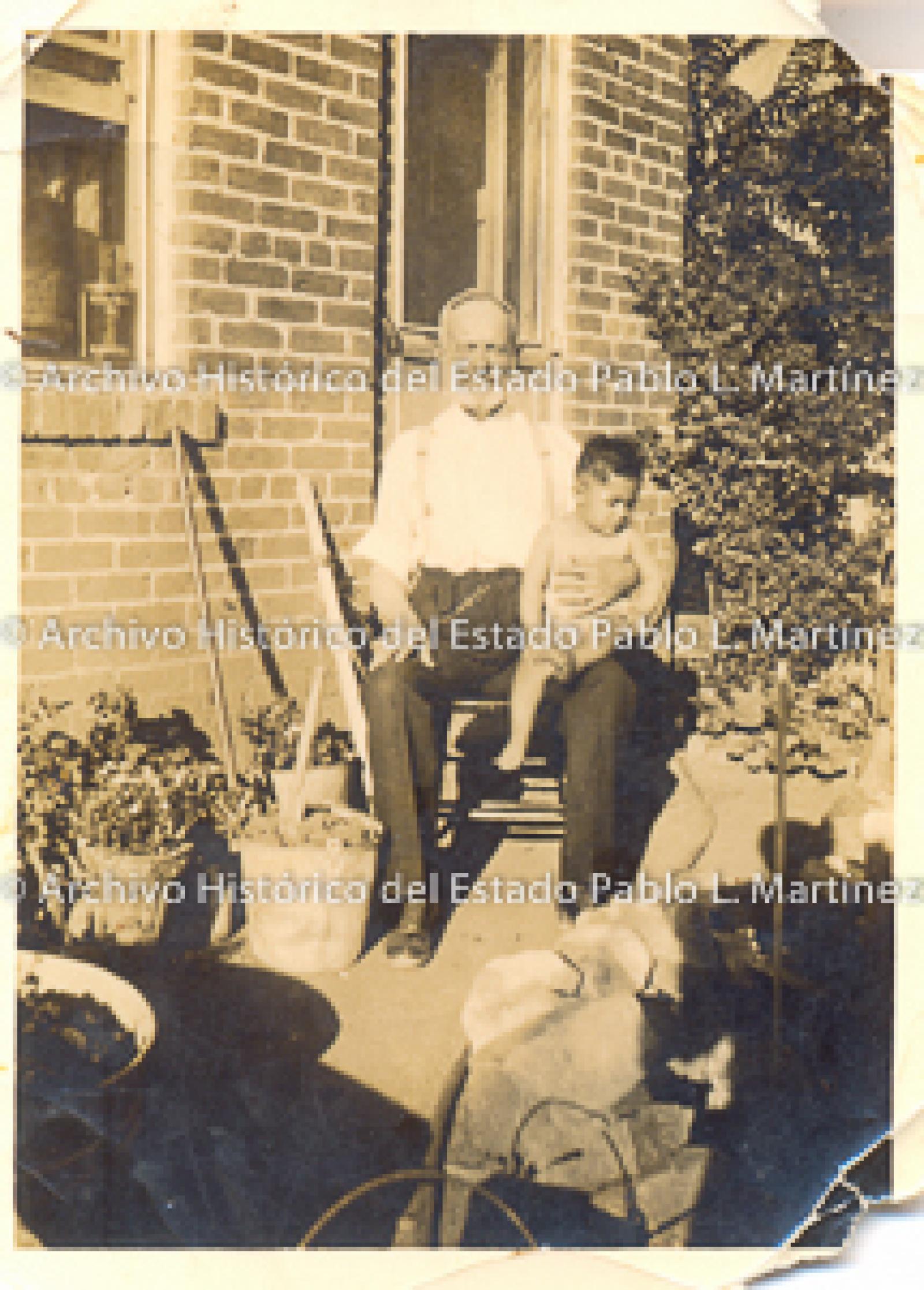 Anciano y niños sentados frente a casa de ladrillos.