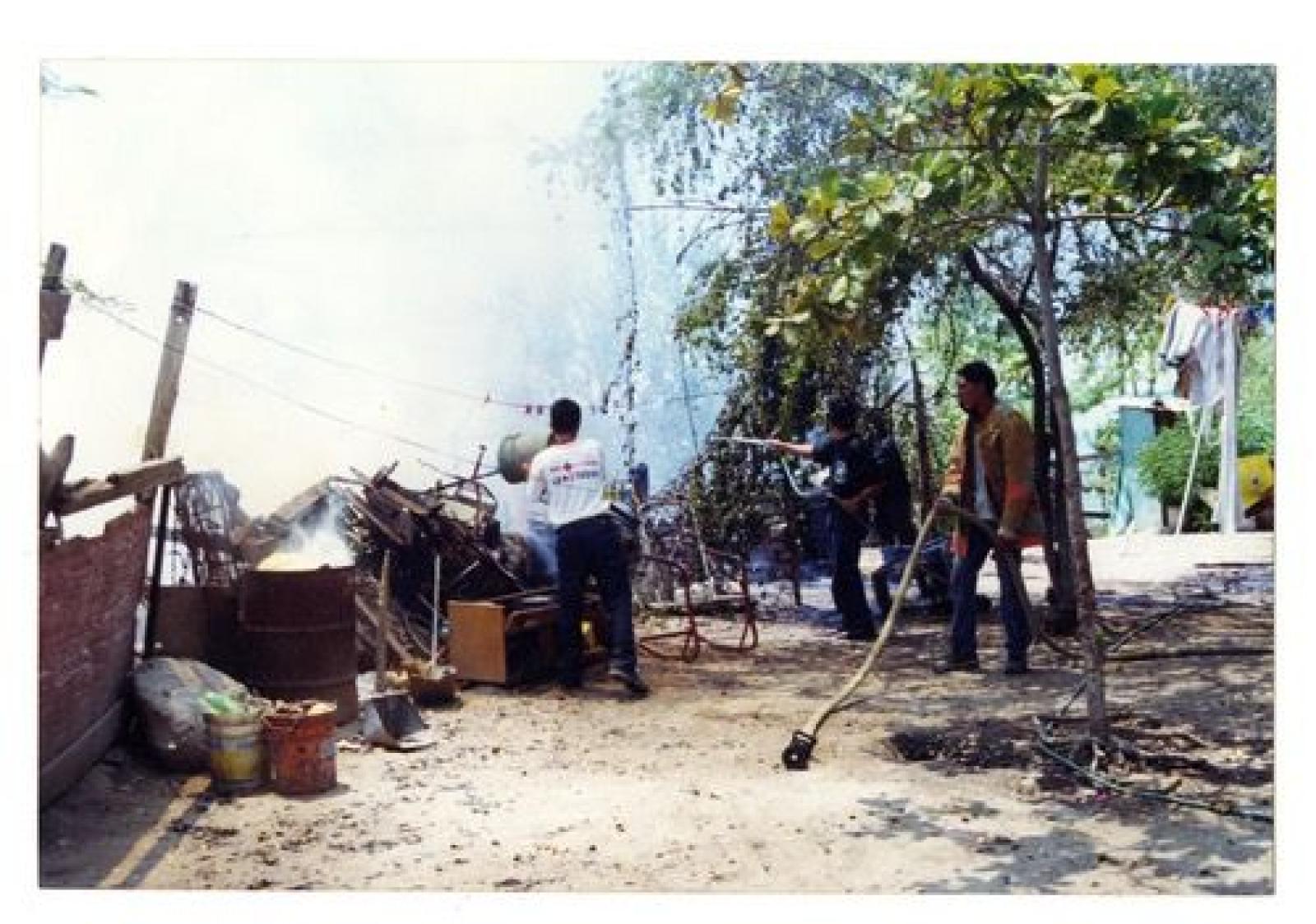 Bomberos apagando fuego con baldes y manguera de jardín.