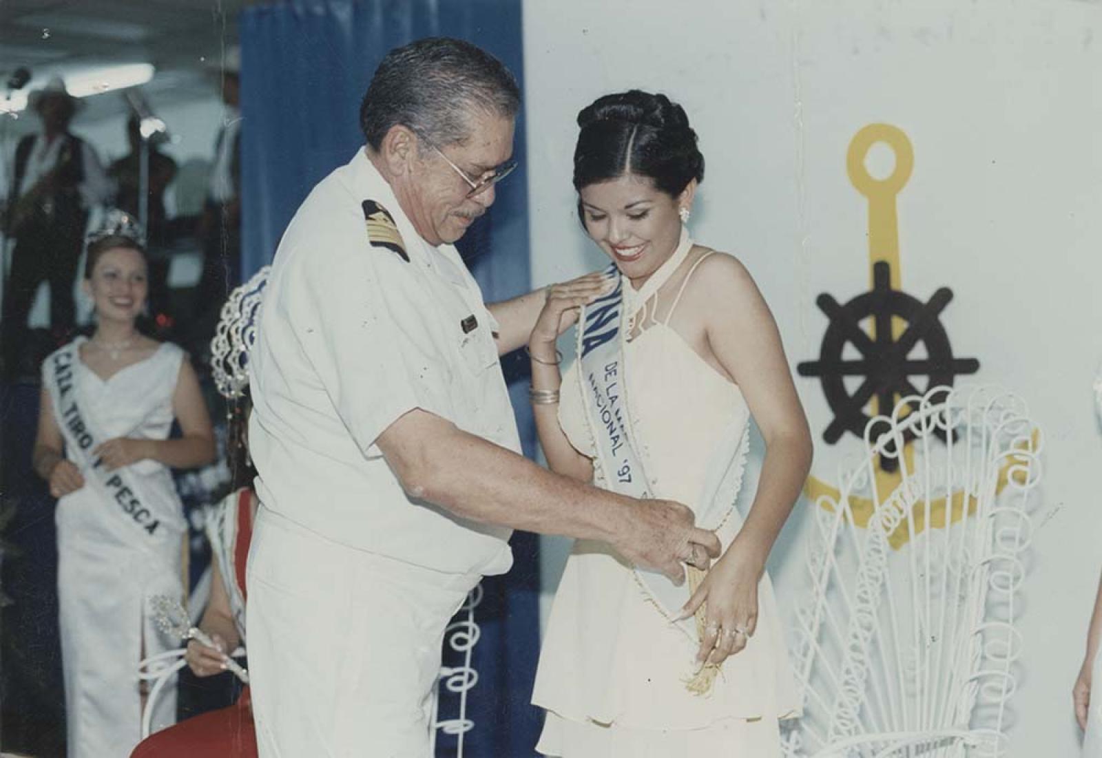 Capitán de la marina coloca banda a mujer.