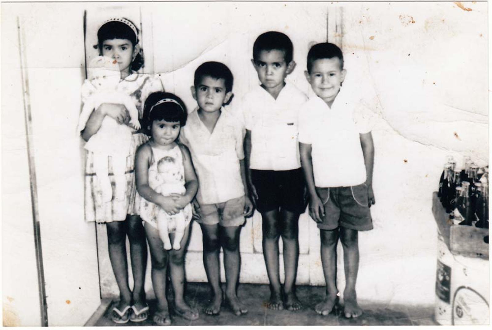 Dos niñas con muñecas, y tres niños de pie.