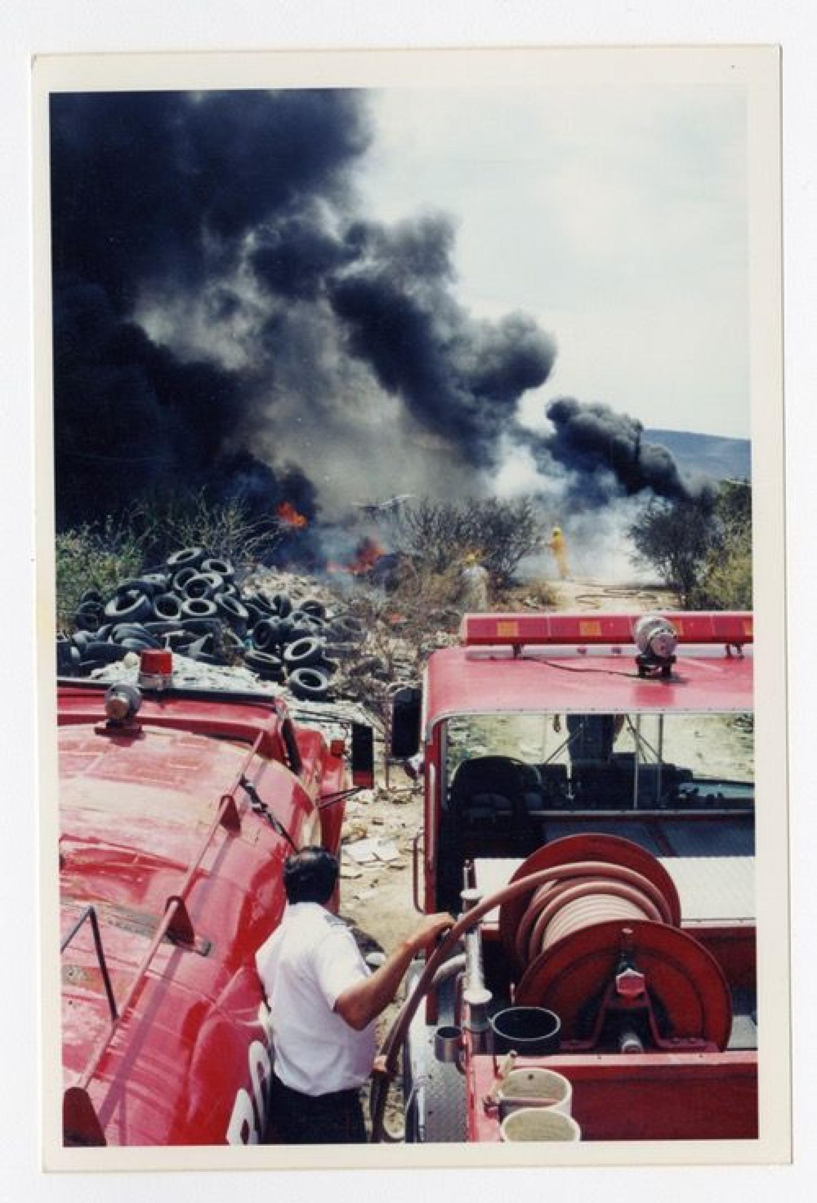 Equipo de bomberos apagando fuego en terrenos con neumáticos.