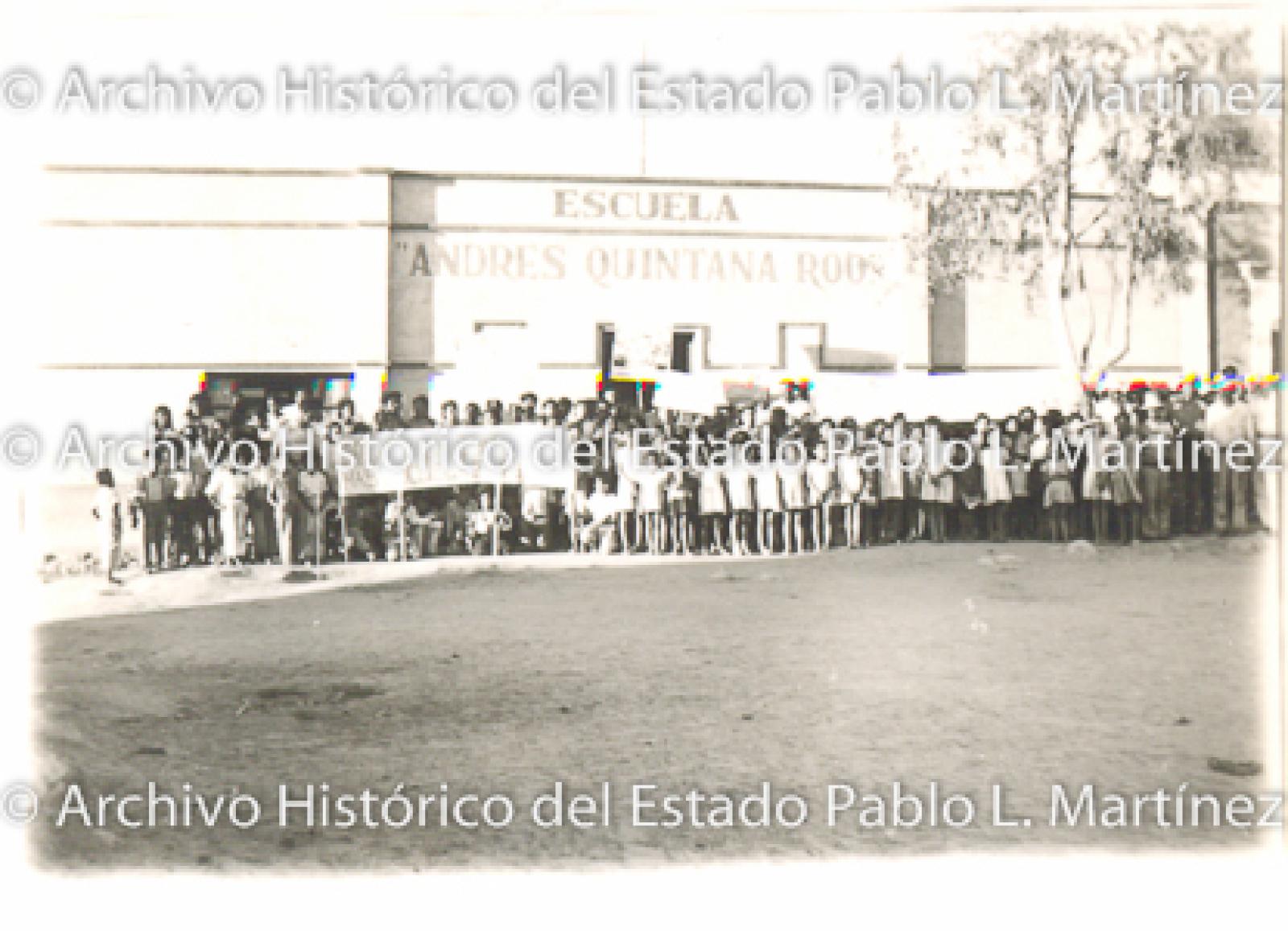Grupo de hombres, mujeres y niños frente a escuela “Andres Quintana Roo”.
