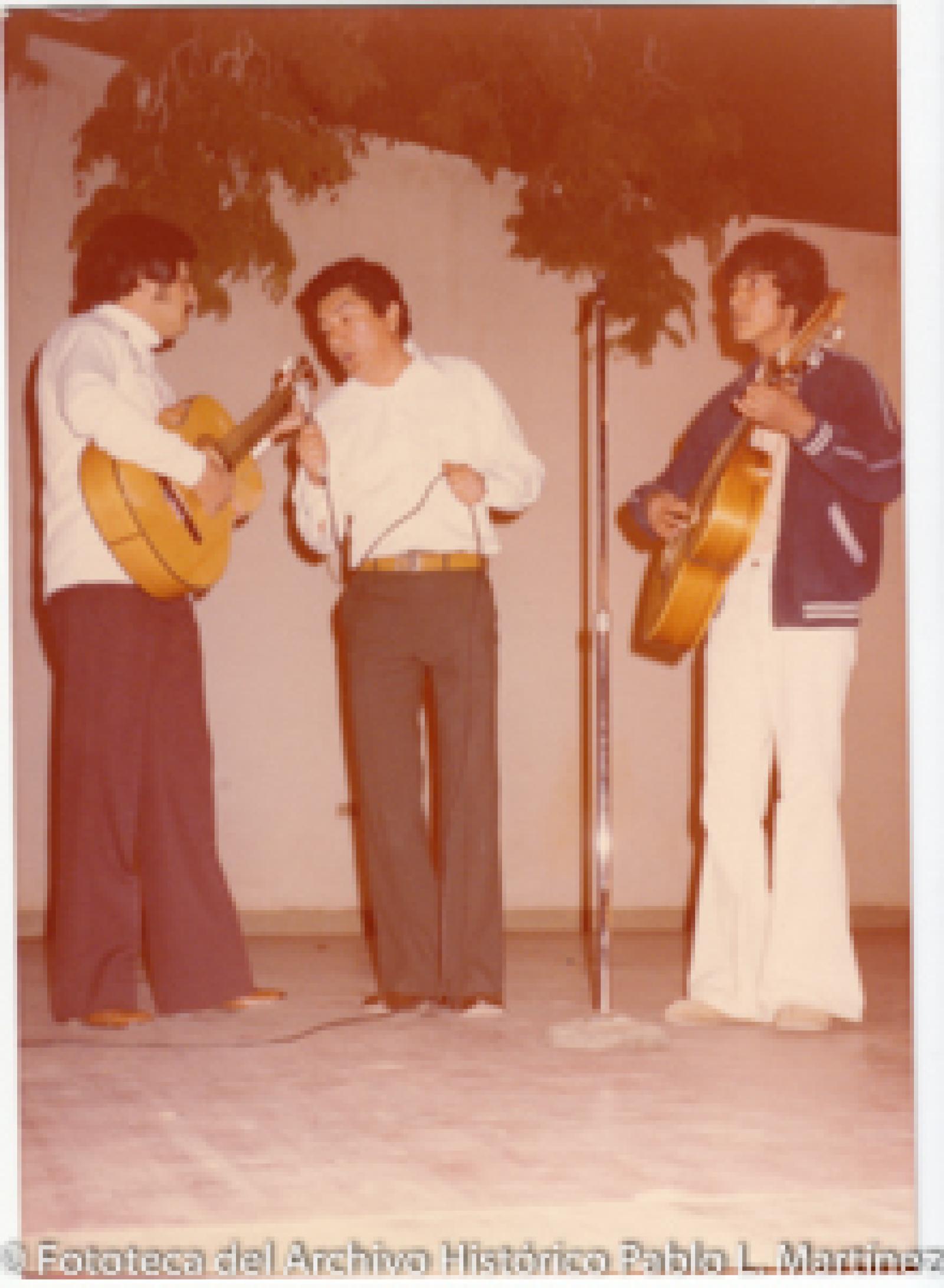 Hombre que canta acompañado de dos guitarristas.