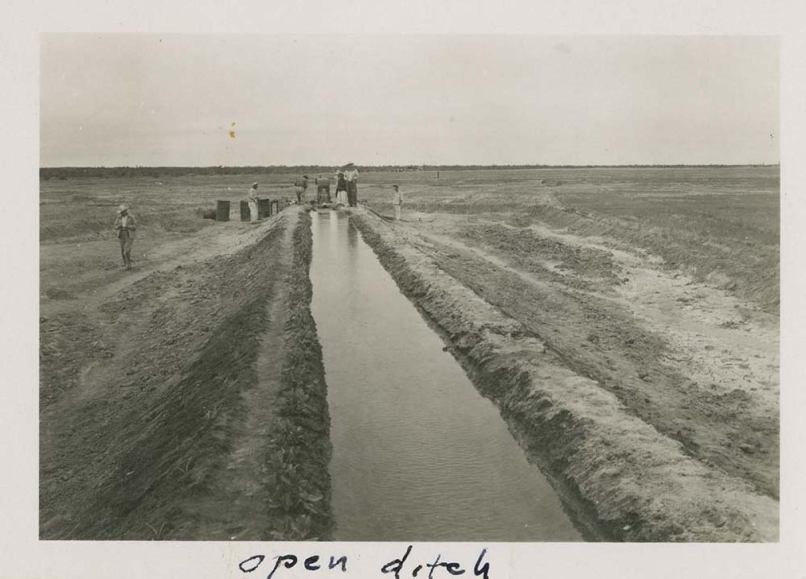 Hombres llenan recipientes con agua de acequia.