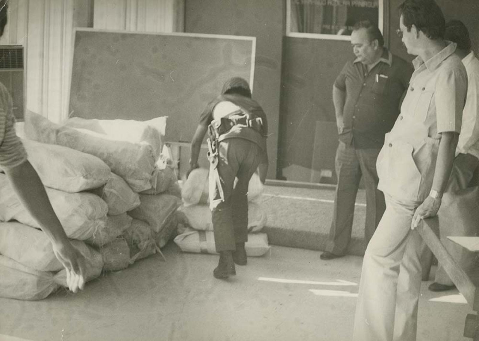 Hombres observan a militar que acomoda costales.