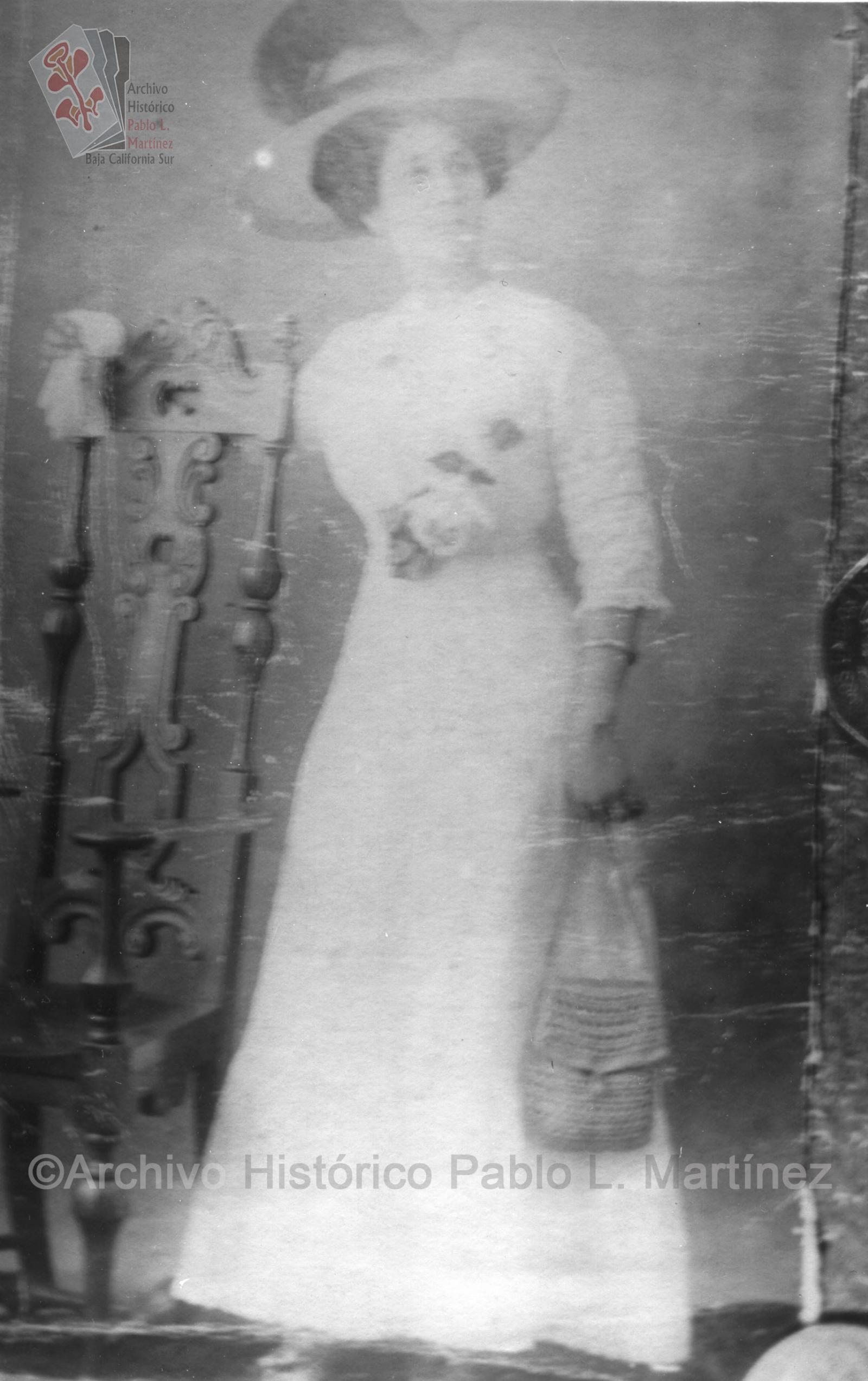 Mujer que viste elegante de color blanco, posa de pie apoyada en silla.