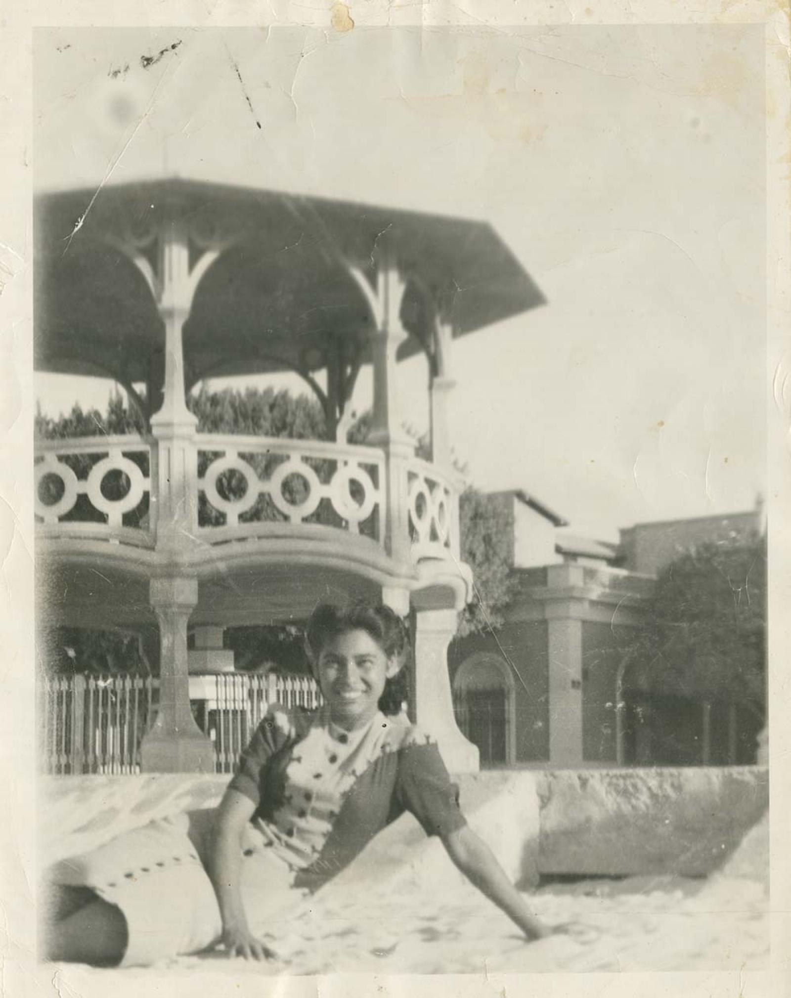 Mujer reposa en la arena de la playa, a su espalda el kiosco del malecón de La Paz, Baja California.