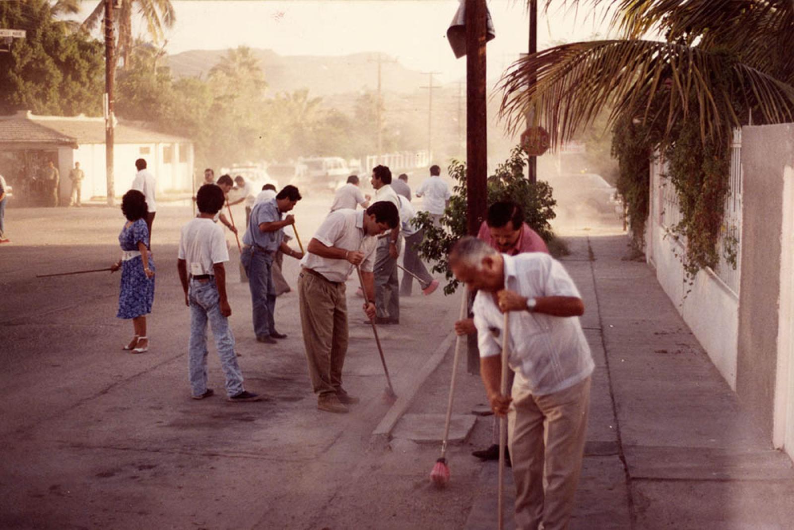 Mujer y hombres barren calles de la ciudad de La Paz, Baja California Sur. Participan en jornada de limpieza.