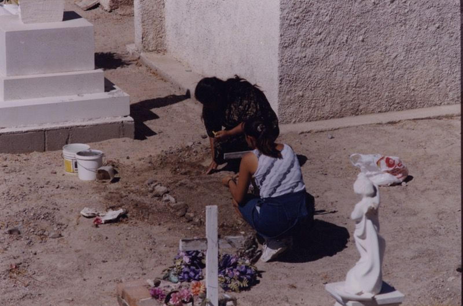 Mujeres acomodan tierra de tumba.