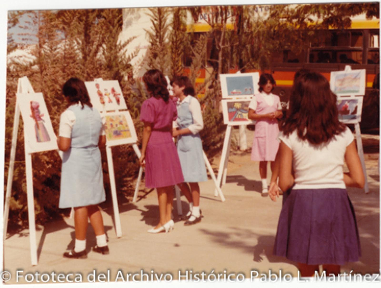 Mujeres con uniforme escolar en exposición de obras artísticas
