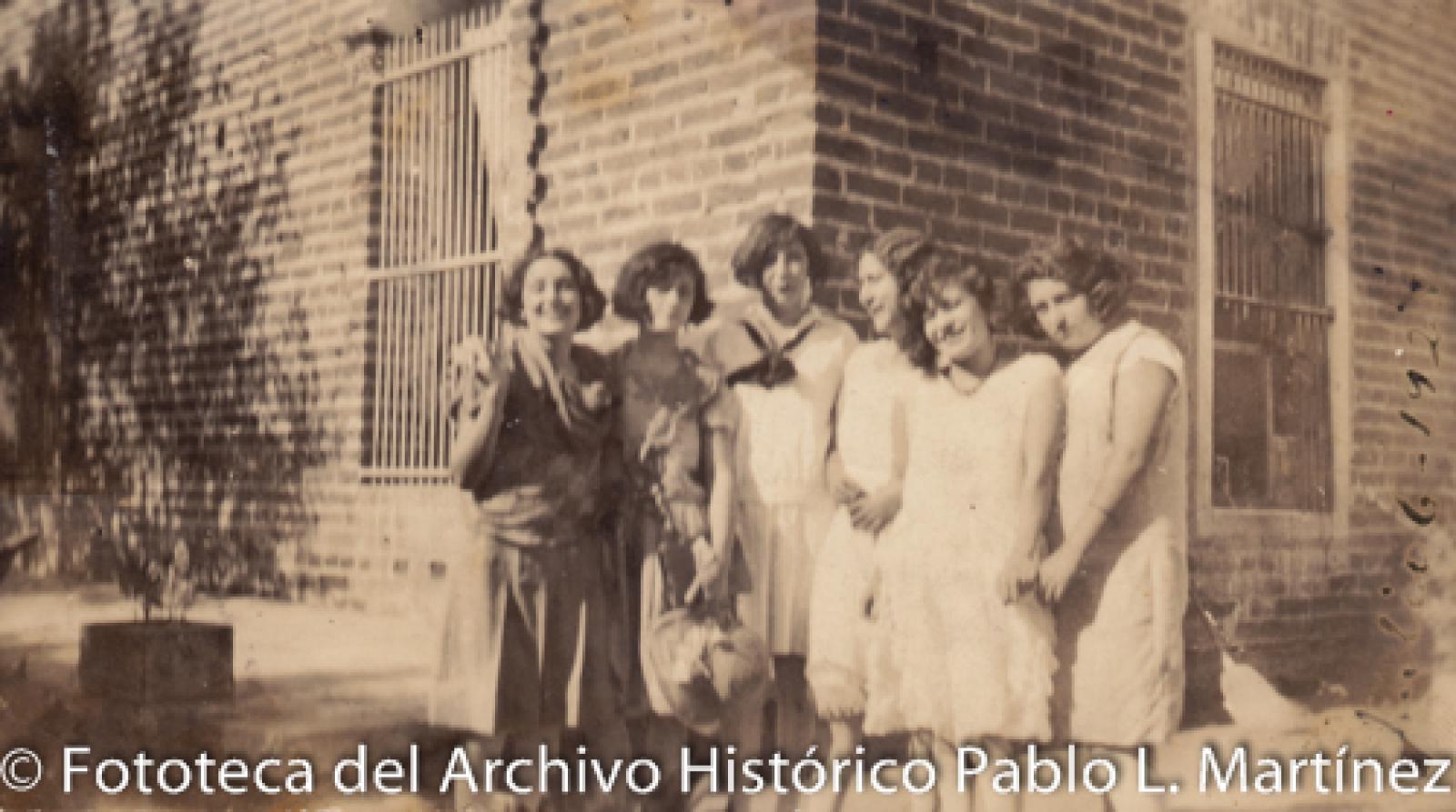 Mujeres frente a casa de ladrillo y ventanales.