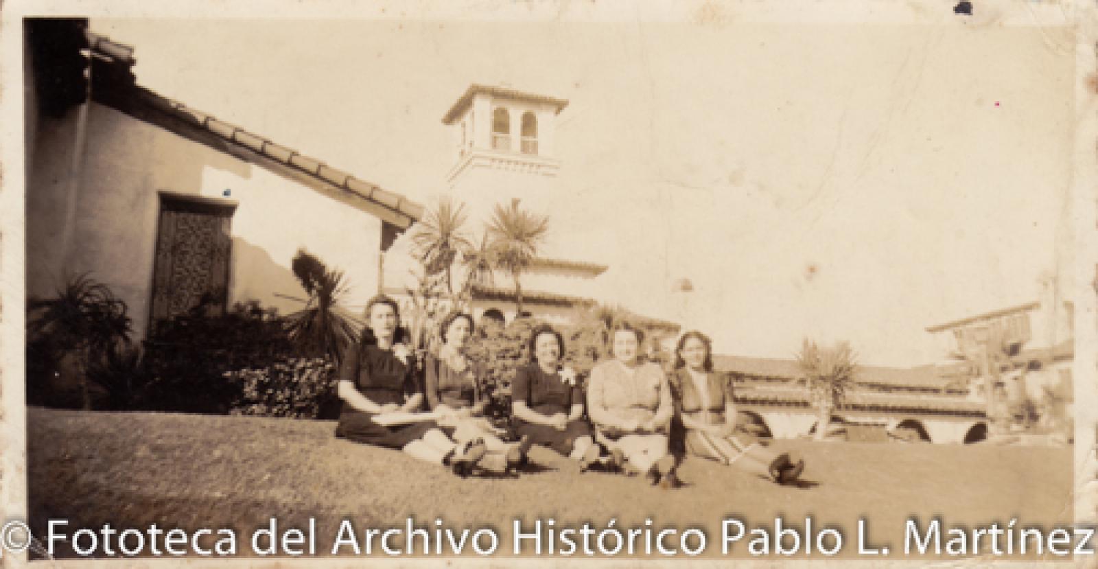 Mujeres frente a casa y jardín.