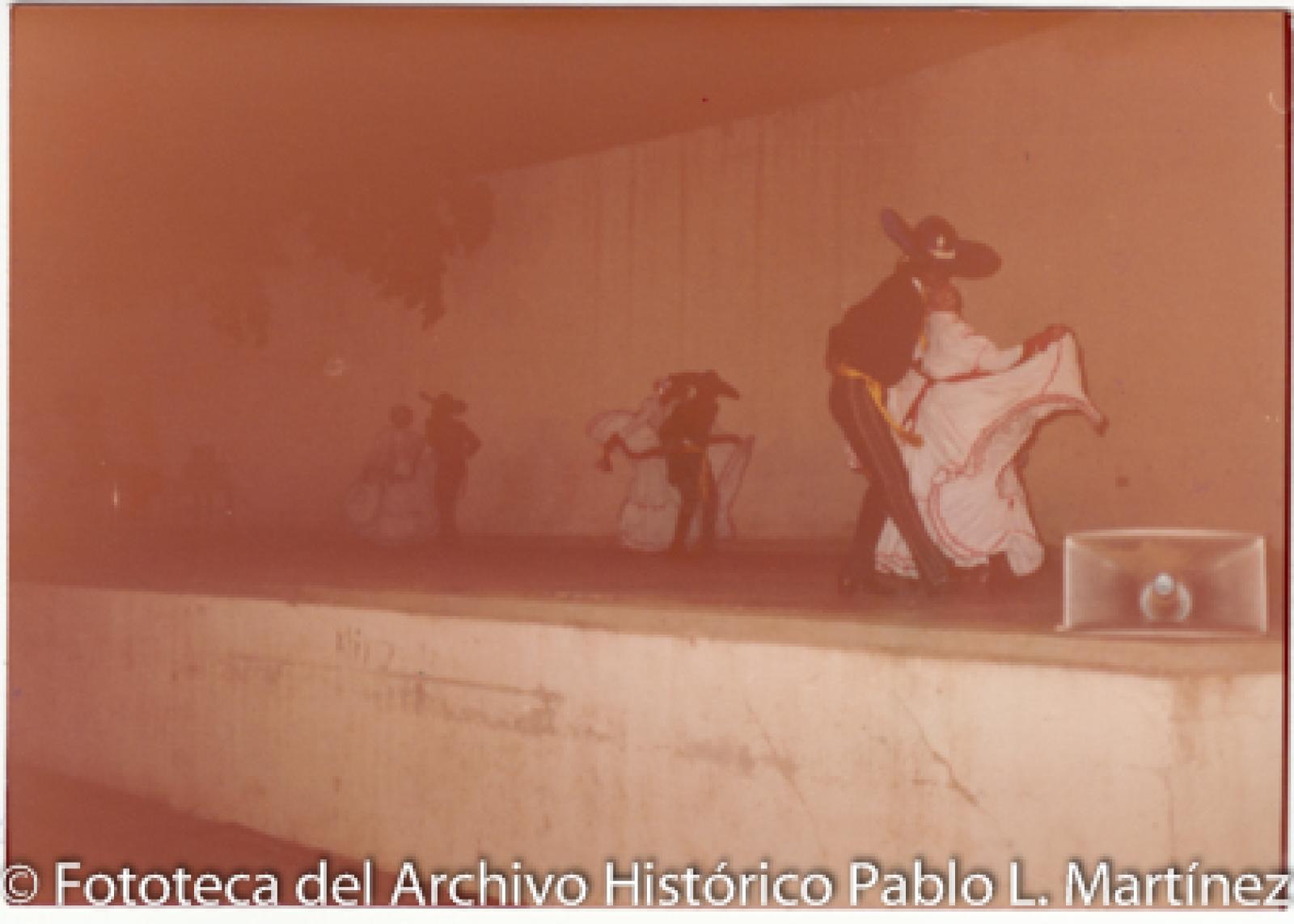 Mujeres que bailan con hombres que visten trajes de charro sobre escenario.