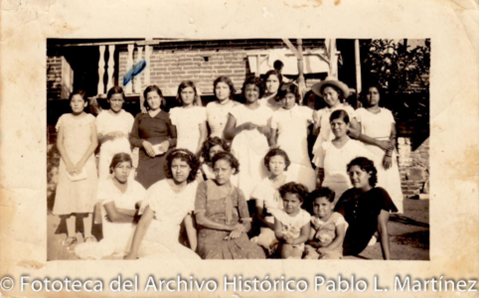 Mujeres y niños frente a casa de ladrillo.