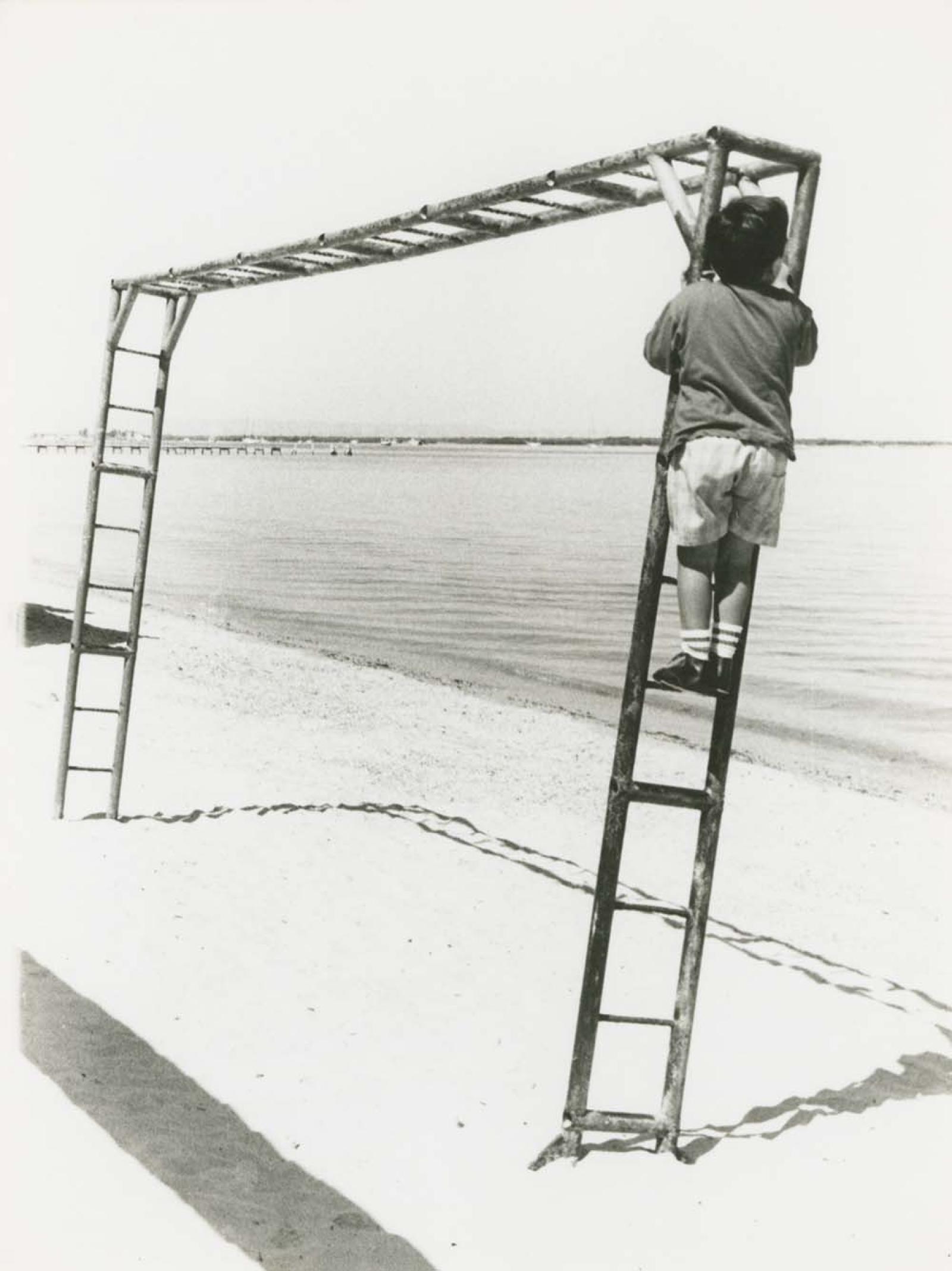 Niño que juega en pasamanos, frente al mar.