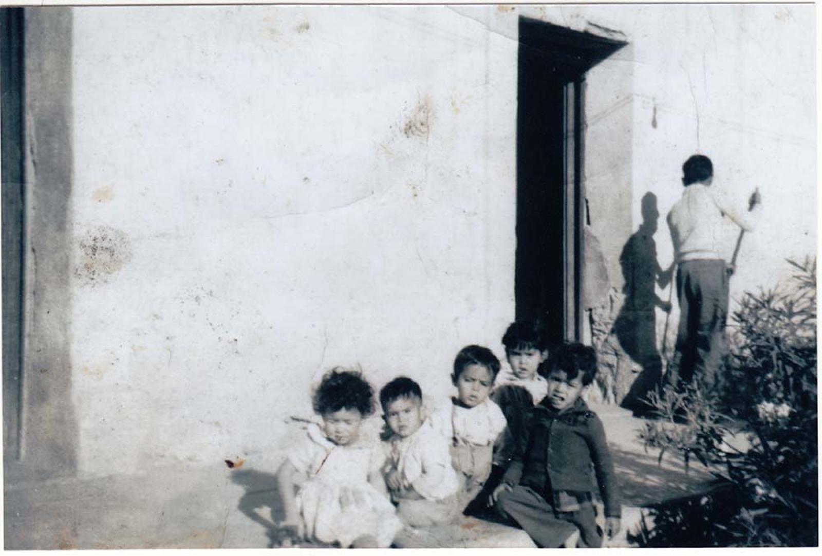 Niños en banqueta, a su espalda un niño que barre.