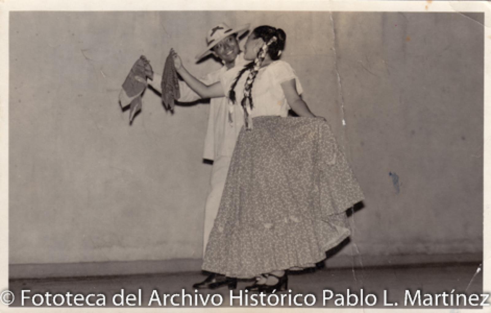 Pareja que viste traje típico mexicano y baila con pañuelos.