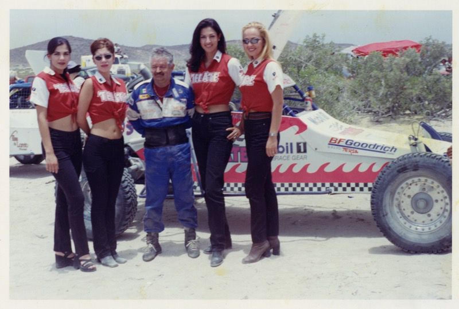 Piloto y edecanes con auto deportivo al fondo.