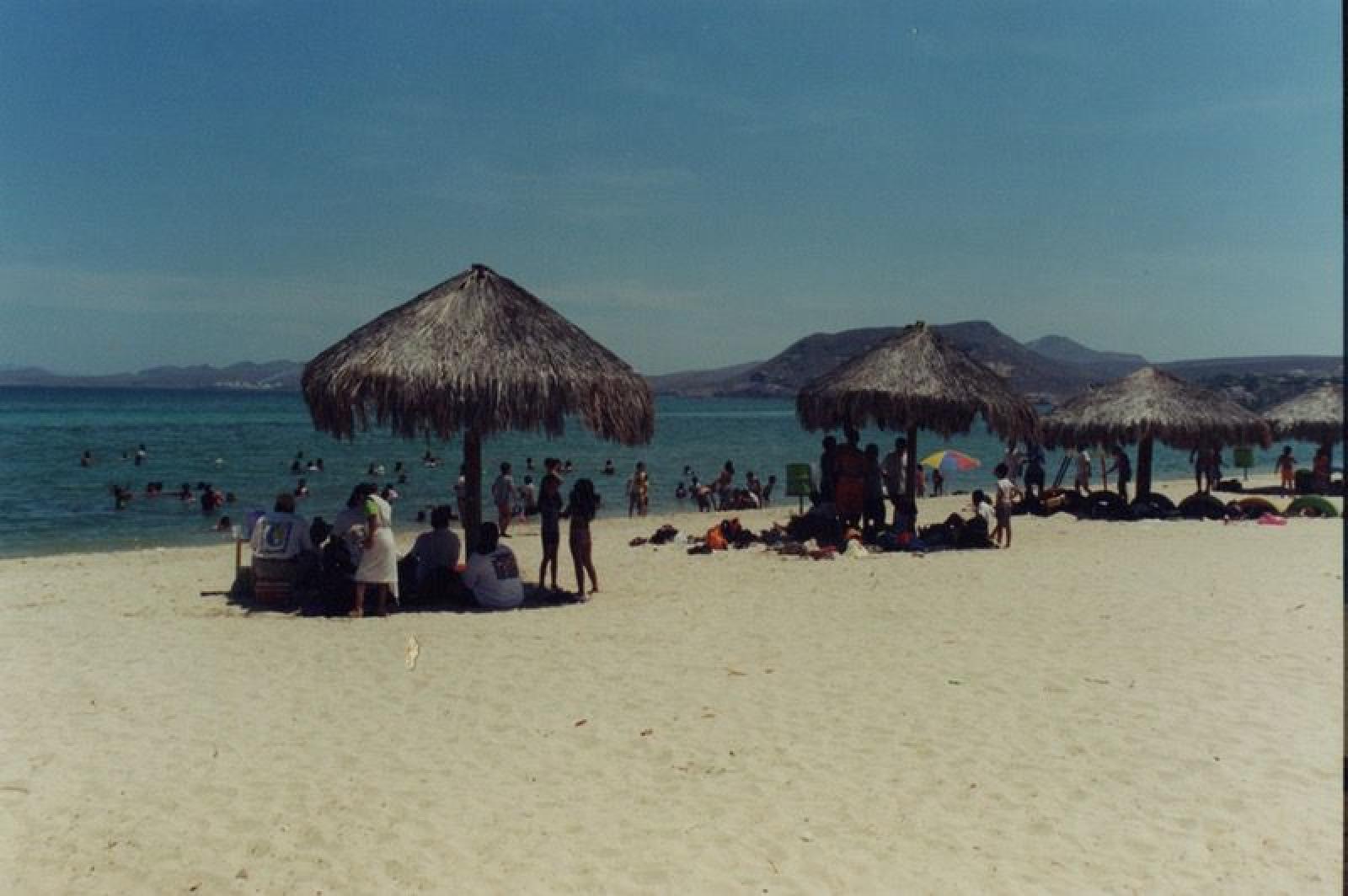 Turistas en playa con palapas.